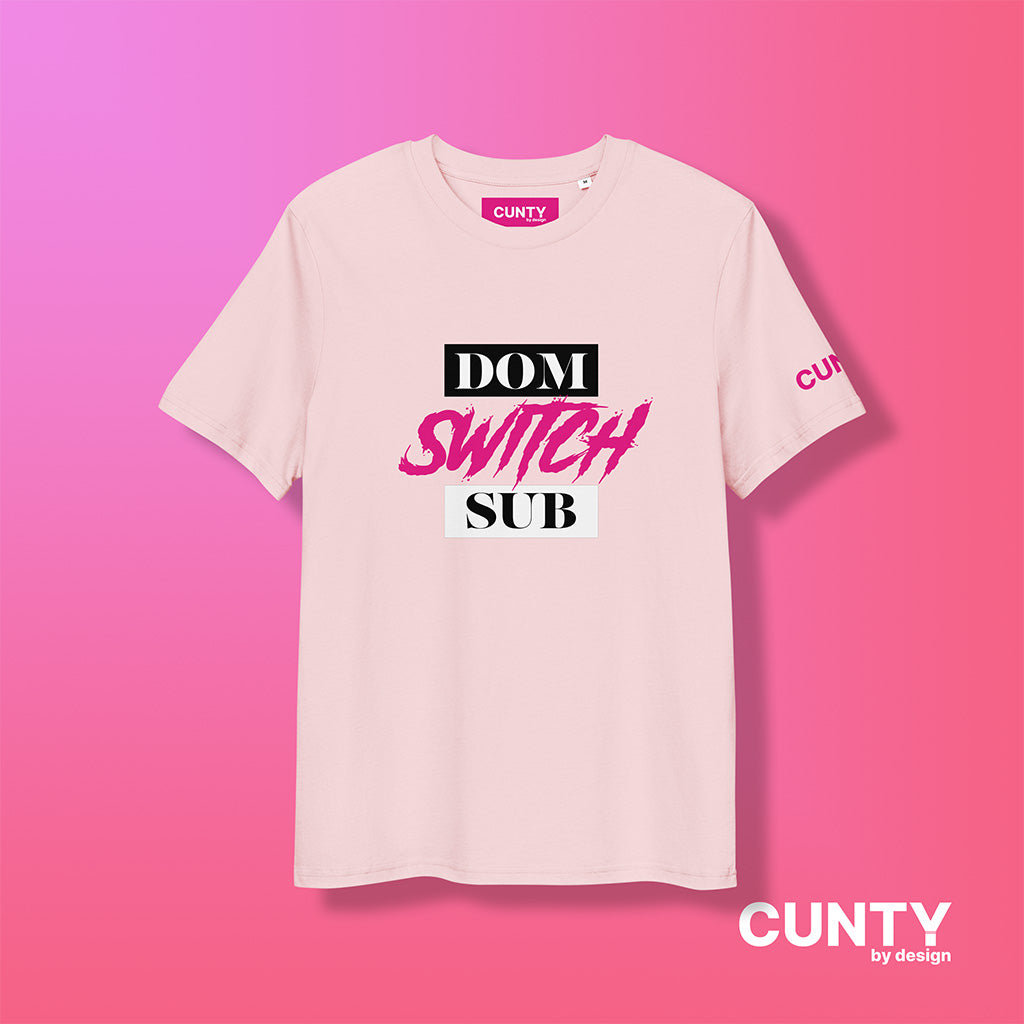 Cotton Pink organic cotton t-shirt featuring the bold text Dom, Switch, Sub in black, white and vibrant pink. The shirt has a unisex design with a Cunty by Design logo on the sleeve, and inside neck label displayed against a fuchsia background.