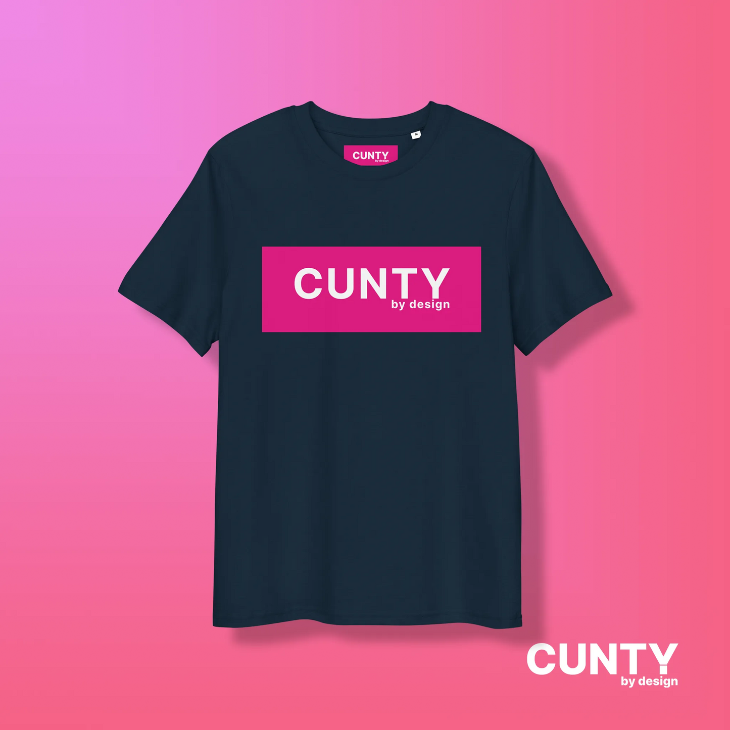 French Navy with Fuchsia Design: A navy blue unisex t-shirt highlighting the "Cunty by Design" logo in a vibrant fuchsia rectangle, against a pink gradient background.
