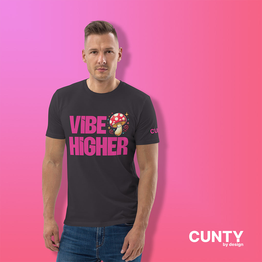 Man wearing an anthracite organic cotton t-shirt featuring the bold text "Vibe Higher" in vibrant pink, paired with a colorful magic mushroom graphic. The shirt has a unisex design with a Cunty by Design logo on the sleeve, and inside neck label displayed against a fuchsia background.