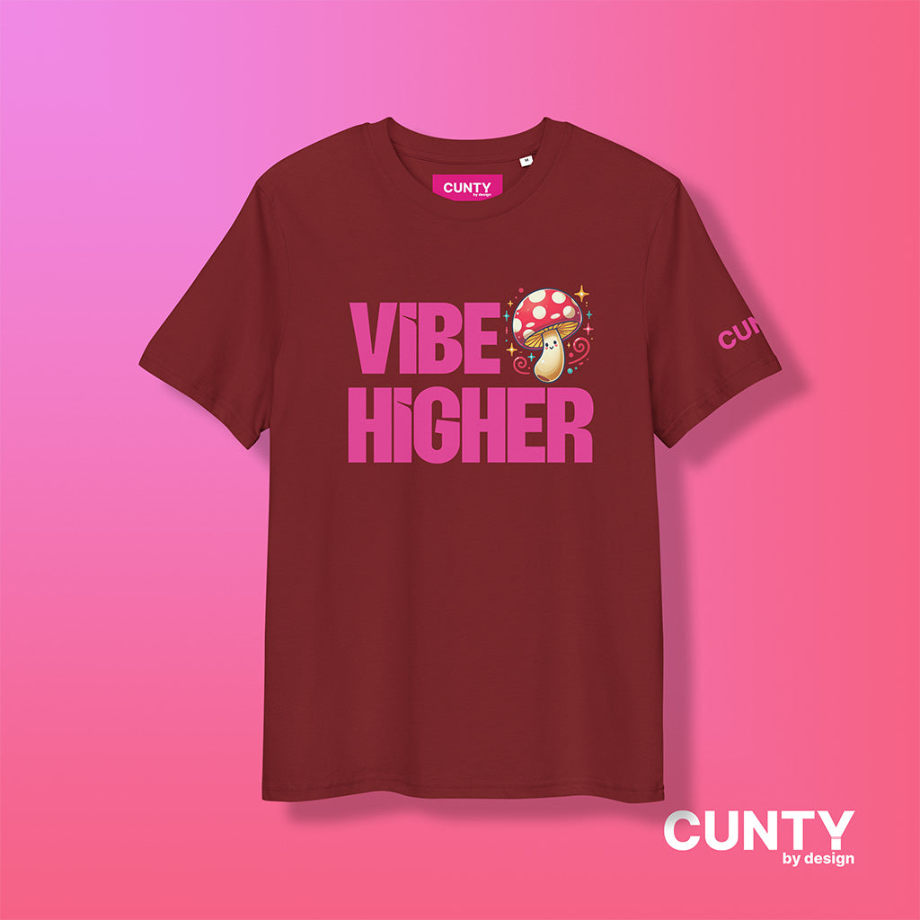 burgundy organic cotton t-shirt featuring the bold text "Vibe Higher" in vibrant pink, paired with a colorful magic mushroom graphic. The shirt has a unisex design with a Cunty by Design logo on the sleeve, and inside neck label displayed against a fuchsia background.