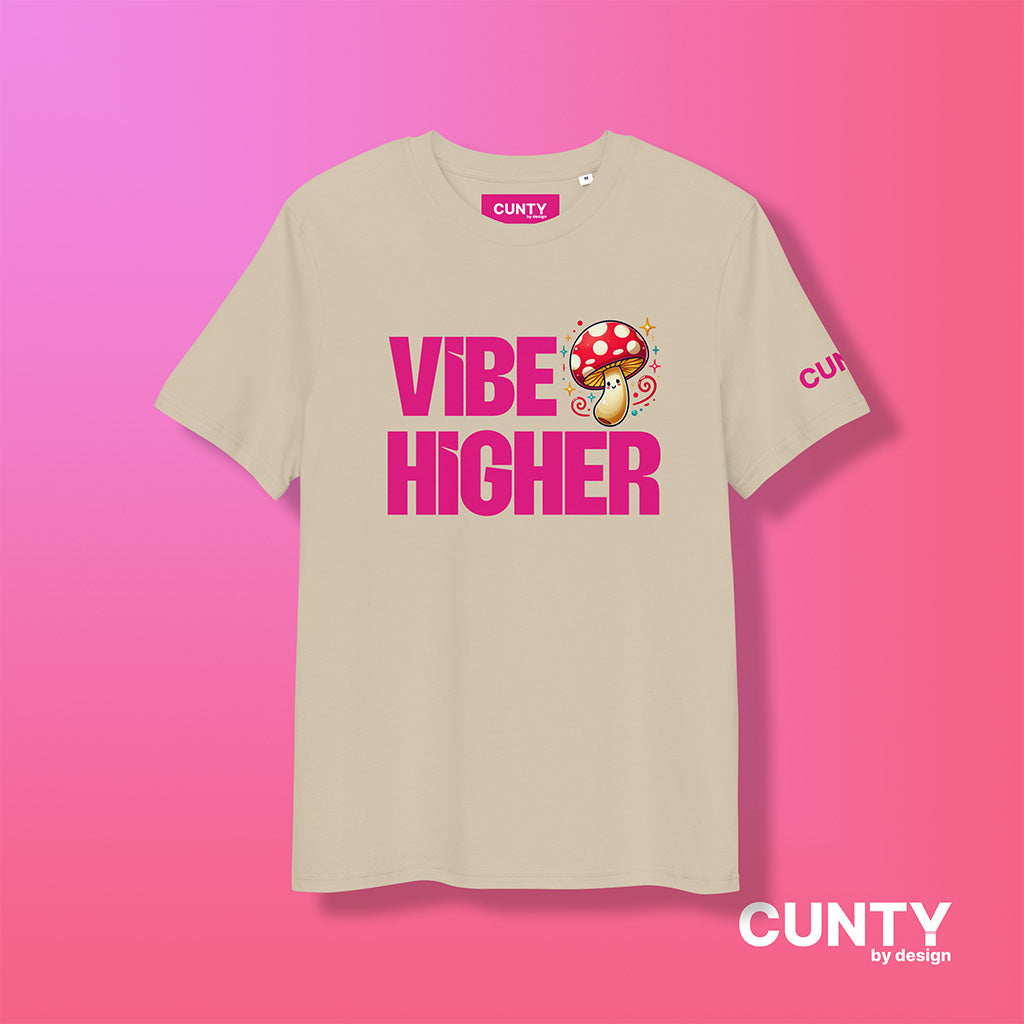 desert dust organic cotton t-shirt featuring the bold text "Vibe Higher" in vibrant pink, paired with a colorful magic mushroom graphic. The shirt has a unisex design with a Cunty by Design logo on the sleeve, and inside neck label displayed against a fuchsia background.