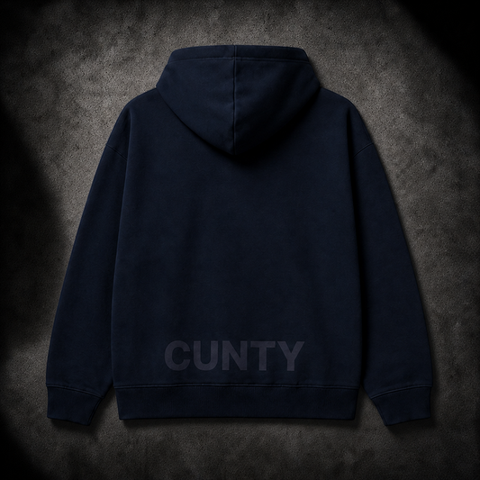 Back of French Navy Blue hoodie with 'CUNTY' tramp stamp logo text on a gray concrete surface